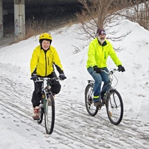 Older man and women biking on a snowy road wearing neon yellow jackets