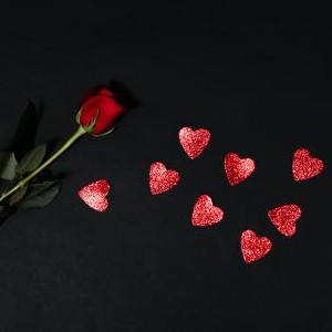 A rose against a black background and sparkly red hearts.