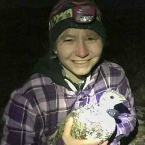 Madeleine Lohman in the dark on a range wearing a headlamp holding a sage grouse.