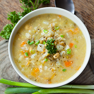 yellow colored soup with vegetables in white bowel with celery stalk underneath
