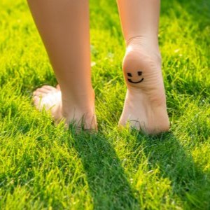 A persons' feet in the grass with a smiley face on the heel.