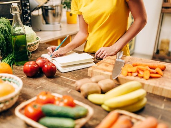 A person preparing a shopping list surrounded by fruits and vegetables.