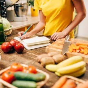 A person preparing a shopping list surrounded by fruits and vegetables.