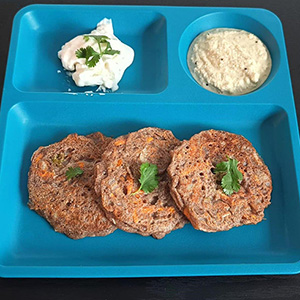 three vegetable pancakes on blue plate with white cream and tan cream on the side. Cilantro garnish on top.