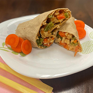 tortilla wrap with vegetables on plate with sliced carrots on side.