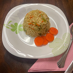 scoop of rice with vegetables on plate with sliced carrots on side