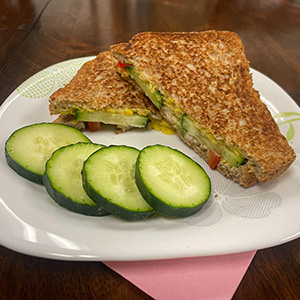 grilled sandwich with vegetables and sliced cucumbers on the side