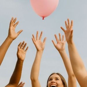 Hands reaching up towards a balloon.