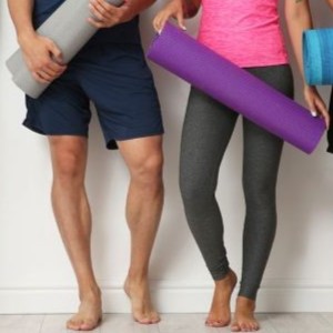 Two people holding yoga mats standing against a wall.