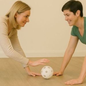 Two participants holding a plank position facing each other while rolling a ball back and forth.