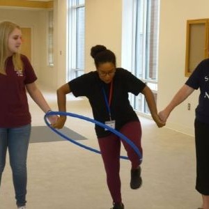 Three women holding hands trying to get through a hula hoop.