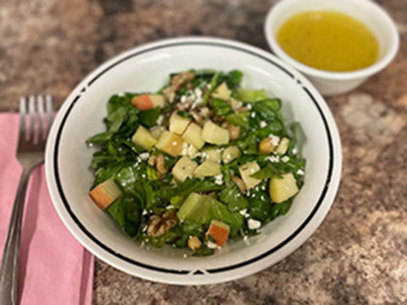 bowl with salad, apple pieces, cheese and small cop with yellow dressing on the side.