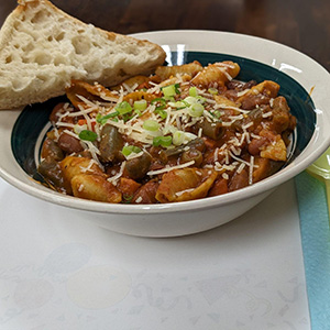 bowl of pasta with red sauce, ground beef, white grated cheese and piece of bread next to it.