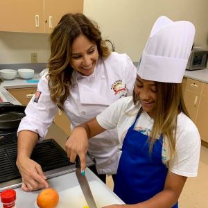 Chef helping young girl cut fruit