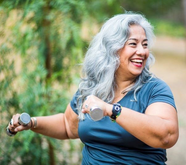 Older women with long grey hair smiling and exercising with hand weights 