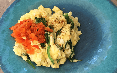 A picture of scrambled eggs, spinach, and red bell peppers on a plate.