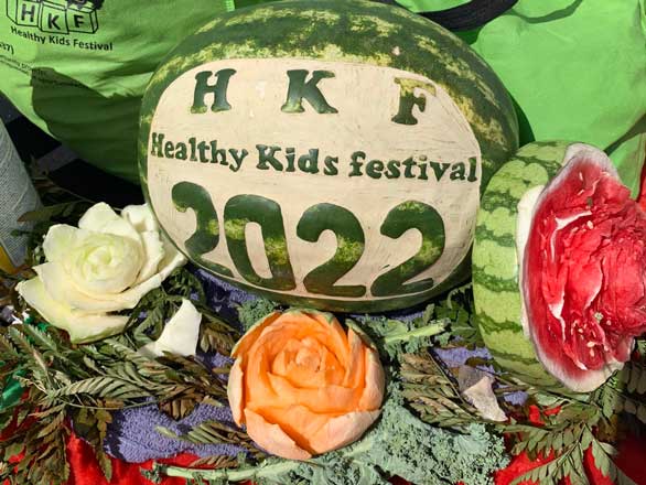 A green watermelon is carved with the letters HKF on top, Healthy Kids Festival in the middle and 2022 on the bottom. 