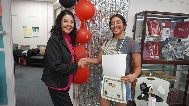 A woman shakes hands with a female teenager holding a certificate. 