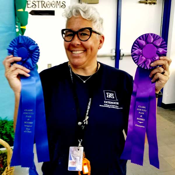 Woman in Navy shirt with Extension logo smiles with blue and purple ribbons. 