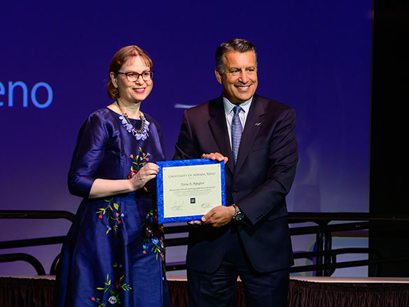 A woman in a blue dress smiles next to a man in a dark suit as they pose with a certificate.