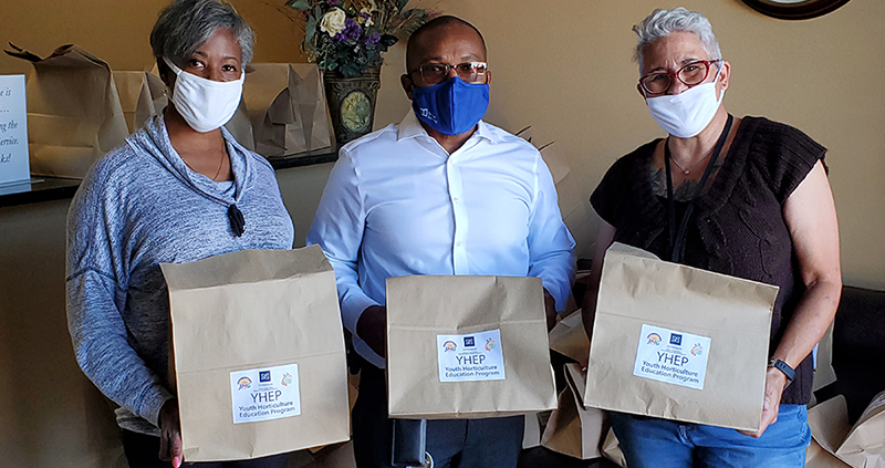 Three masked people holding full brown bags that feature Extension branding.