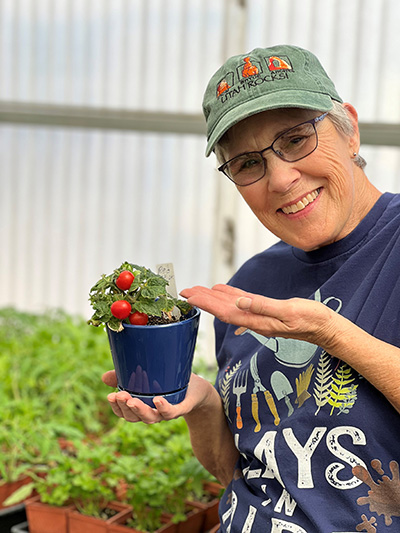 A person wearing glasses and a hat holding a plant and smiling at the camera.