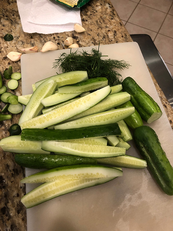 Bunch of cucumber spears on a white cutting board on a granite counter top.