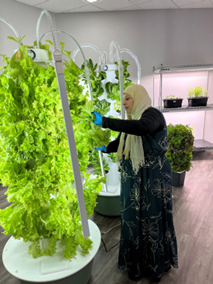 A woman touching plants growing on a lit tower garden.