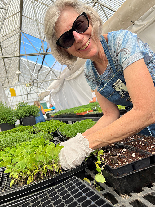 A person smiling with sunglasses around plants.