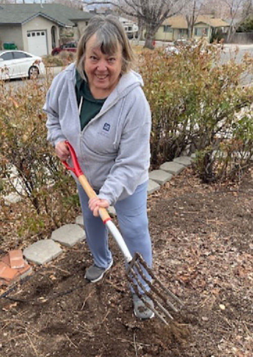 A person holding large rake outside in front of a house.