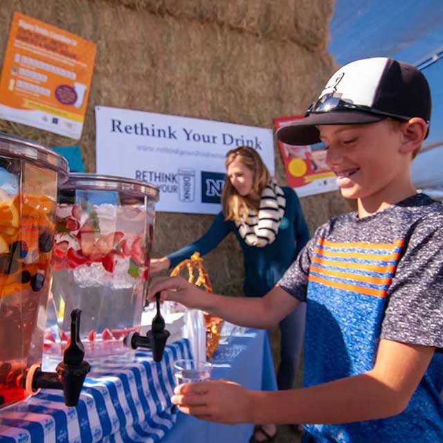 A boy pouring a glass of fruit-flavored water from a pre-prepared pitcher.