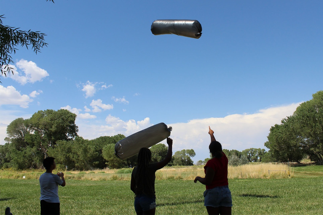 Three youth point up at two solar balloons they are flying outside.
