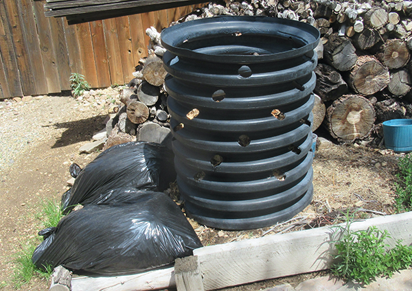 A black barrel with holes and two black trash bags on the ground.