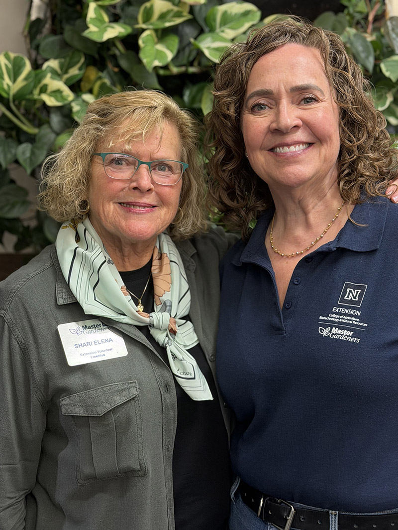 A person smiling with sunglasses around plants.