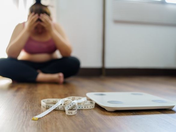 A woman looking upset over weight on scale.