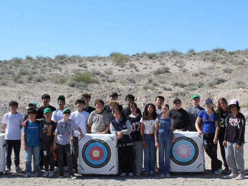 A group of kids standing in an archery field with targets