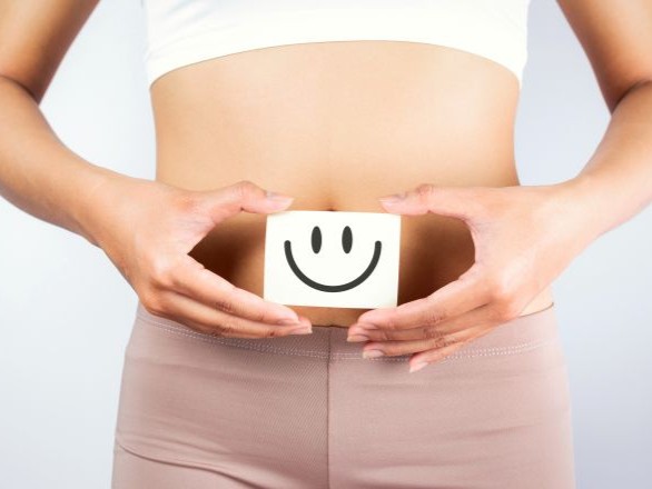 Person holding a smiley face in front of belly.