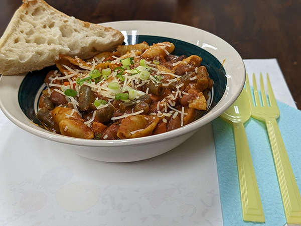 bowl of pasta with red sauce, cheese on top and piece of bread on side. Yellow silverware on the side.