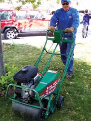 A drum aeration machine is pushed by a man working on a commercial lawn.