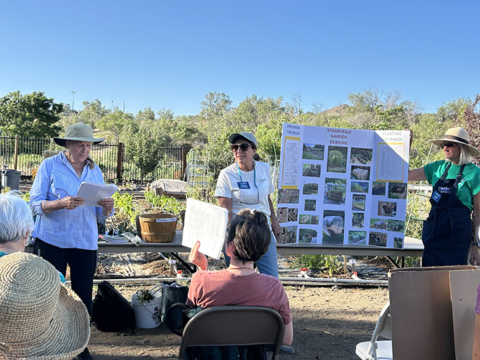 Three people standing in front of outdoor tables and a sign with pictures with people sitting in chairs