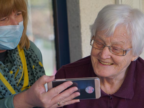 Older adult looking at phone with an individual wearing a mask