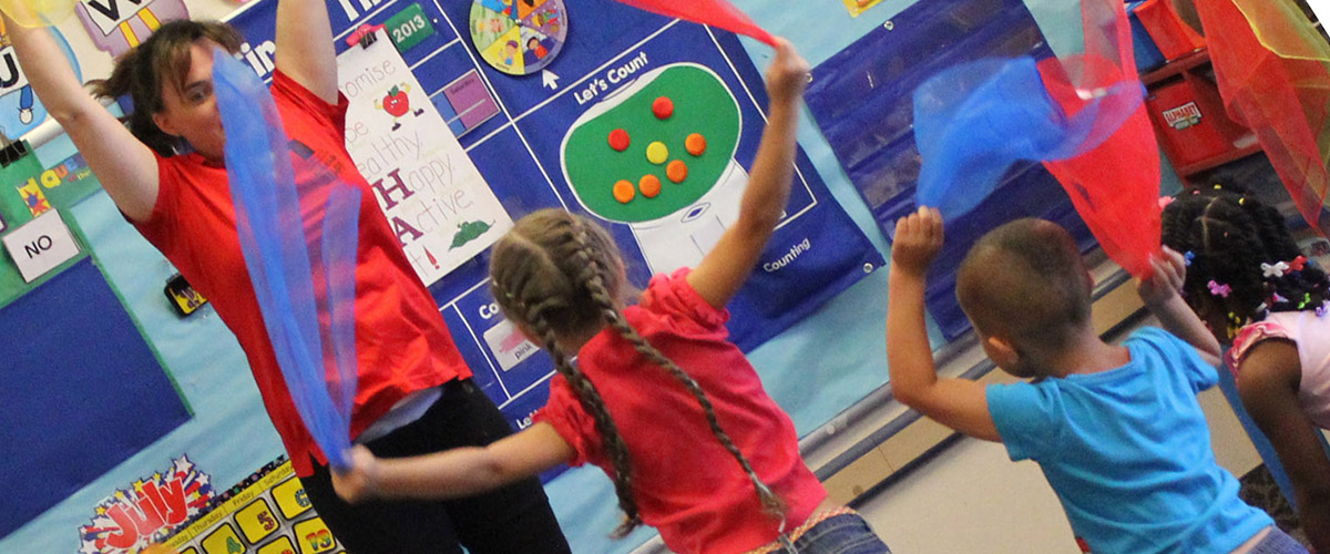 Kids and teacher dancing with colored scarves in a classroom.