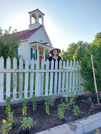 Photo of a woman smiling standing behind a white picket fence in front of a white house.