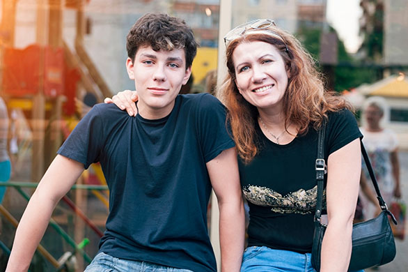 teen son and mother sitting side by side and smiling