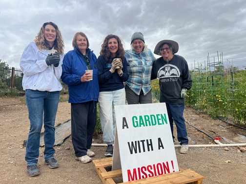 Group of people standing outside standing behind a garden sign.