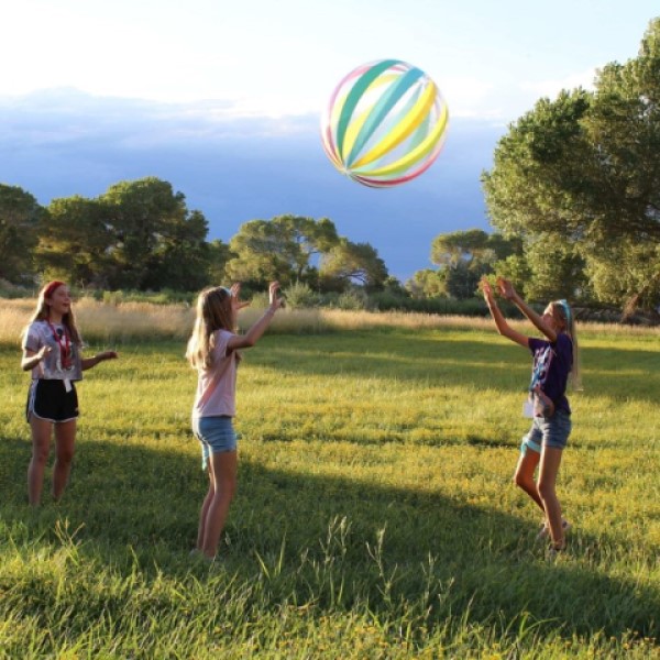 Three girls in a field tossing a beach ball