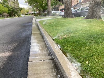 Lawn sprinklers adjacent to a street with water running off onto the street and down the gutter.