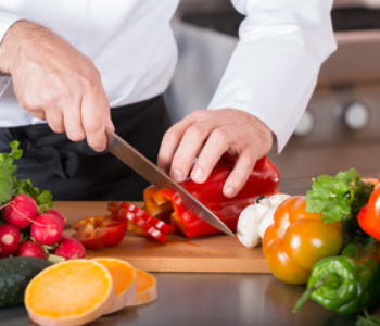 Man cutting red bell pepper with other vegetables near the wooden cutting board