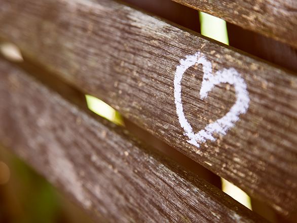 A white chalk heart on a wooden bench.