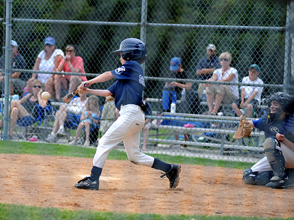 A child attempting to hit a baseball pitch with the catcher reaching out.